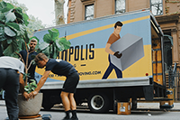 Three men picking up a large tropical plant to put in a moving truck parked on a New York street.