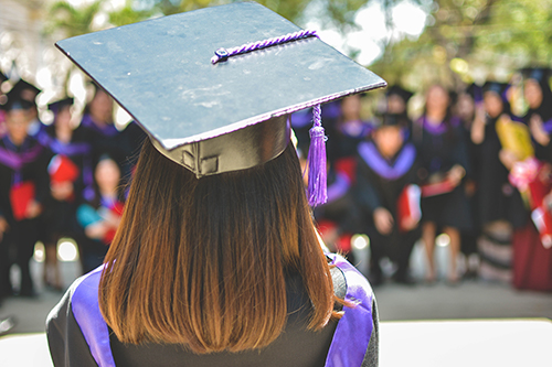 A college graduate facing away from the camera, her black and purple graduation regalia visible