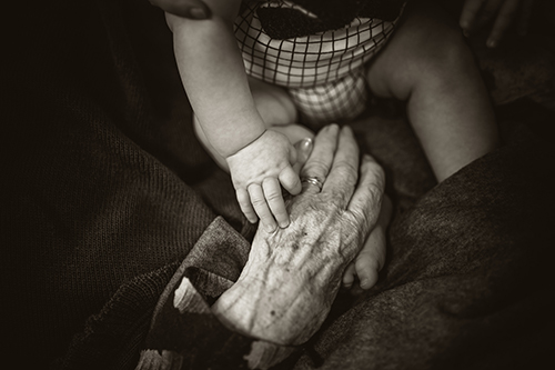a black and white photo of a child's hand holding the hand of an elderly individual